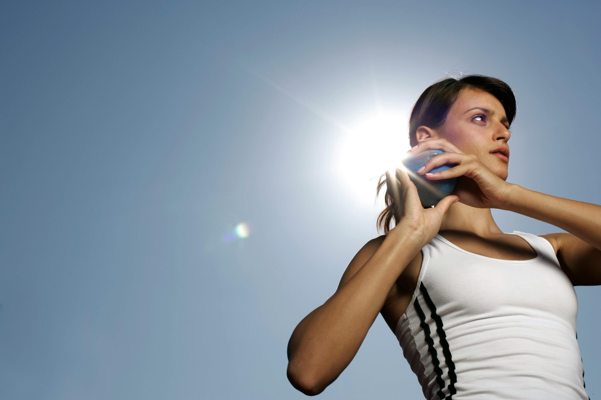 Focused female athlete in sportswear ready for shot put against clear blue sky.